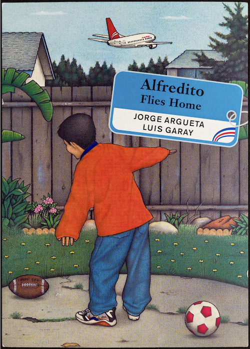 Colorful cover of the children's book Alfredito Flies Home. We see a boy from the back. He is wearing a red long-sleeved shirt and blue pants. He is in a yard with green grass, a fence, and there is a football on a small area of concrete near the grass. He is making airplane shape with arms. The title of the book is written on a luggage tag.
