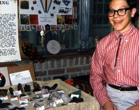 boy in red striped shirt and bolo tie, smiling, with rock collection