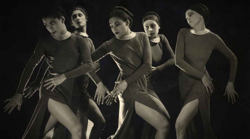 Katherine Dunham and her company in the 1936 work, Fantasie Negre. Black and white photo of five female African American dancers in dark dress posed looking to their right.
